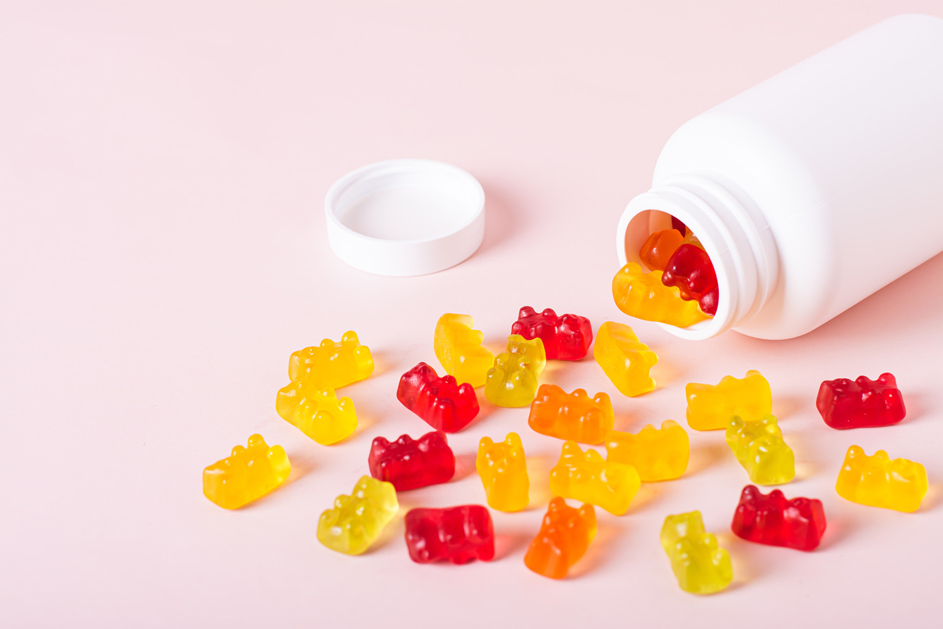 Multi-colored gummy bears spilled from a white supplement bottle
