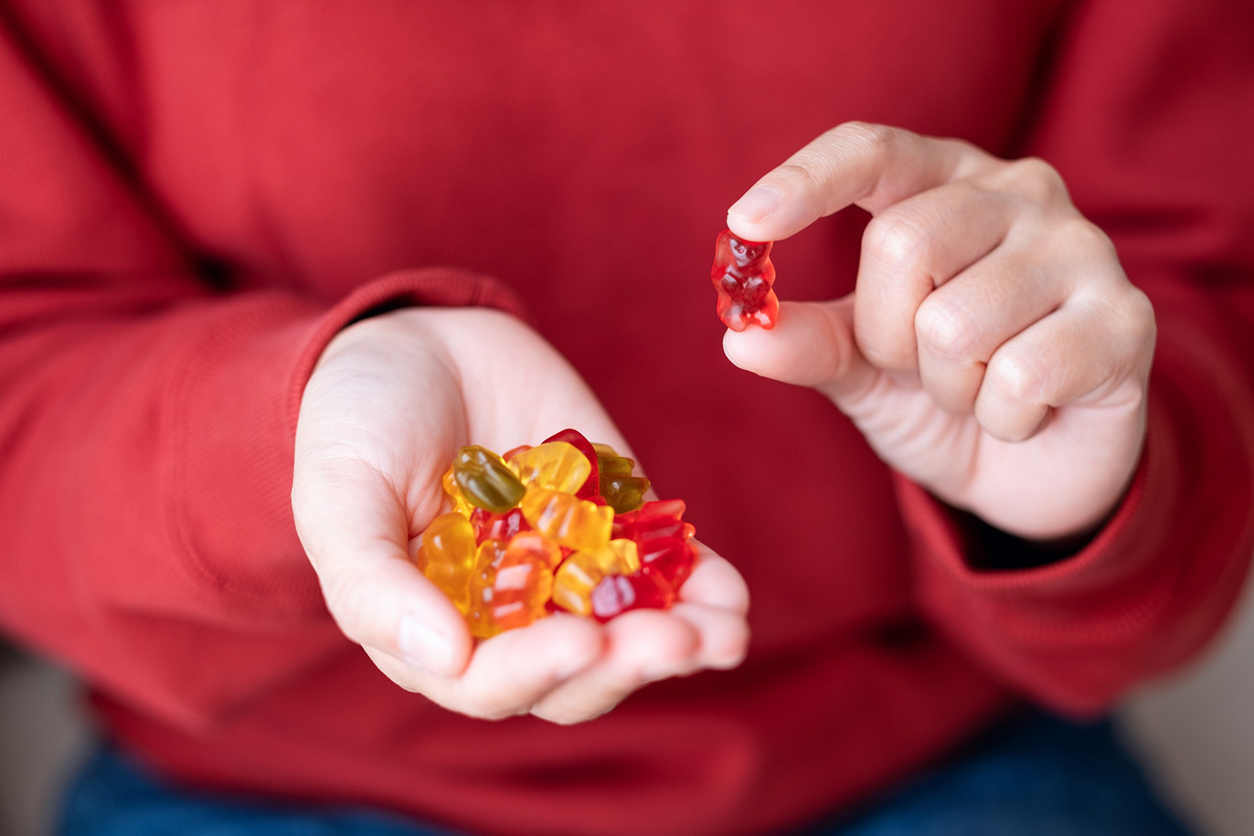 Person in a red sweater picking a single gummy bear from their hand