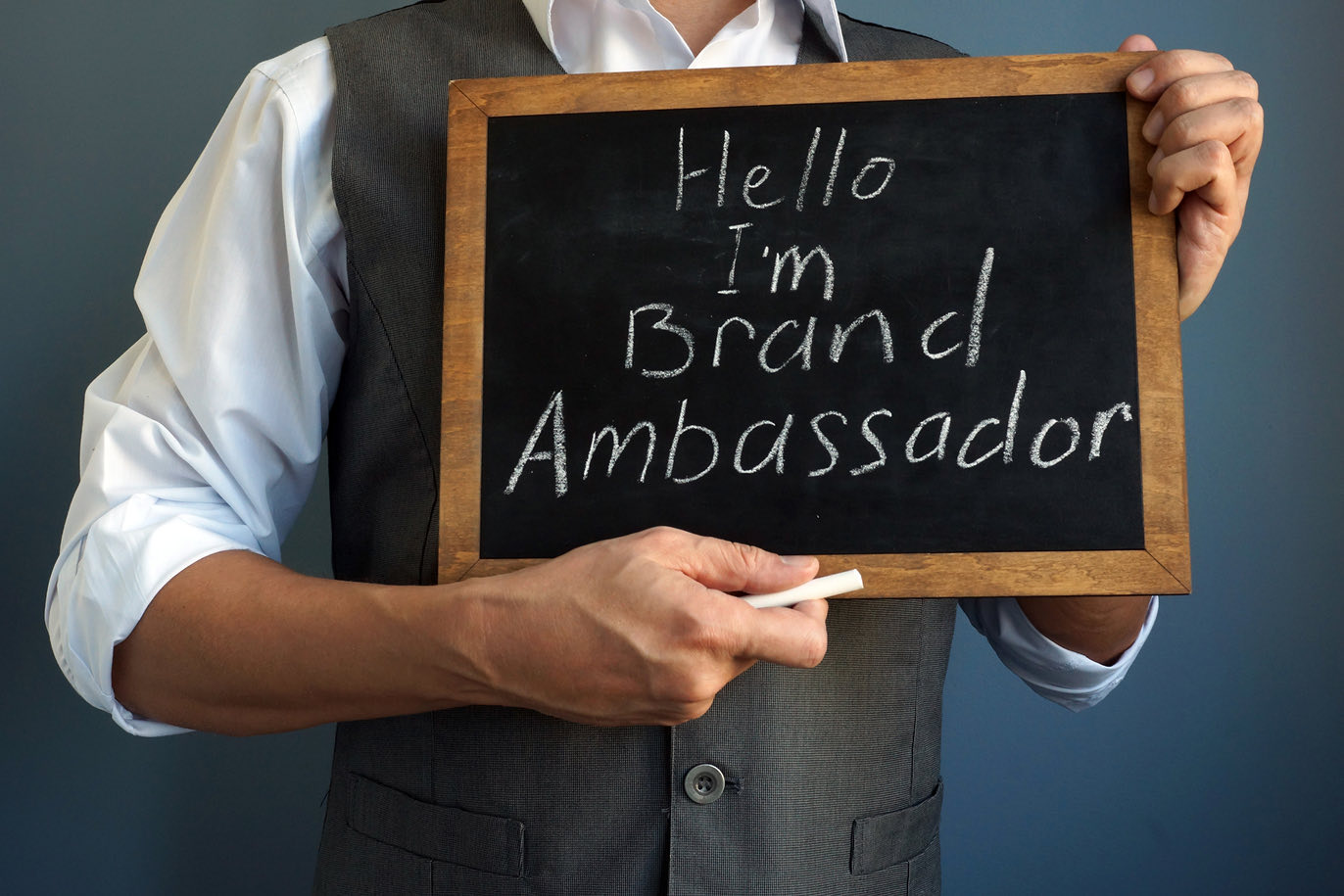 Person holding a chalkboard saying "Hello I'm Brand Ambassador"