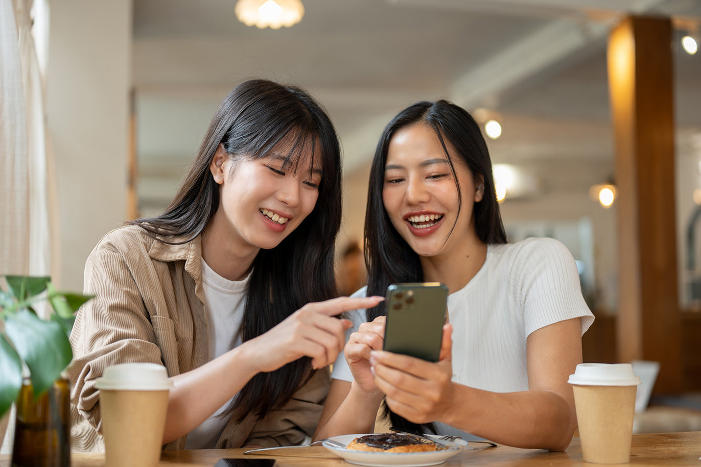 Two friends looking at a smartphone together at a cafe