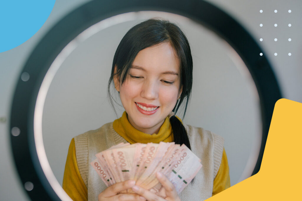 Young woman holding a fan of cash in front of a ring light