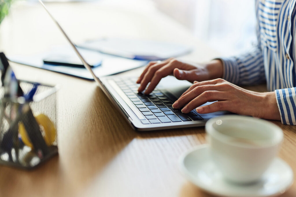 Close-up of hands typing on a laptop at a desk