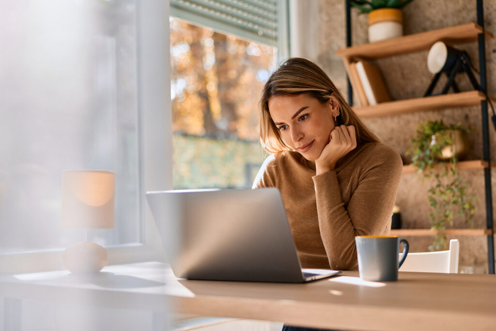 Woman working on a laptop by a window at home
