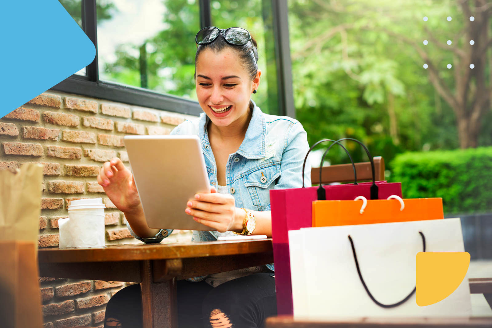 Happy woman with shopping bags using a tablet at a cafe