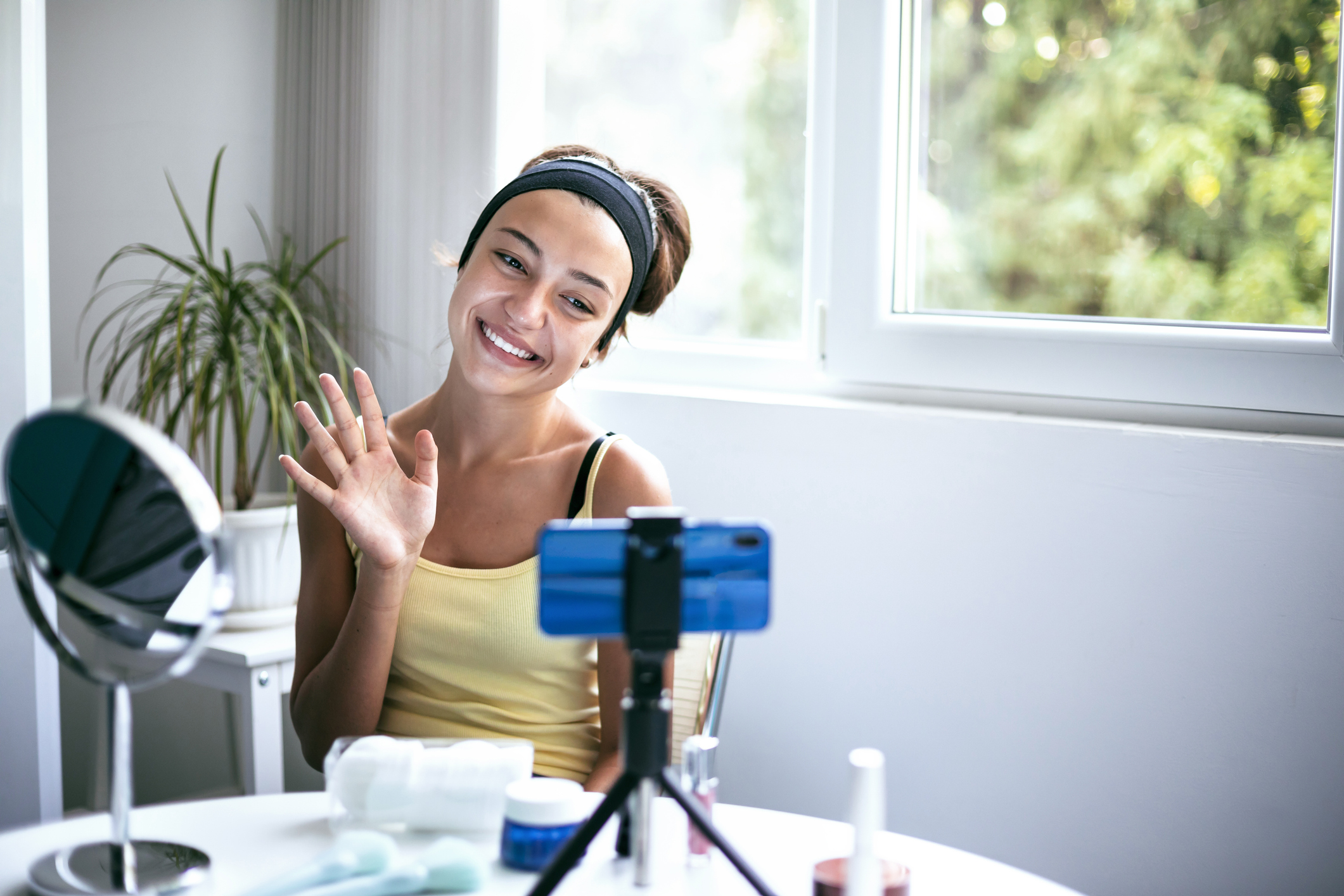 A content creator sits in front of a mirror and phone camera, preparing to share her skincare routine in a bright, cozy space. Ambassador programs.