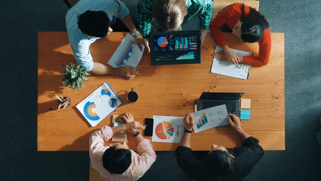Team reviewing pie charts and bar graphs spread across a table, the kind of reporting mistakes an affiliate management system is meant to fix 